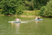 Hier sehen Sie wie 2 Boote mit jeweils 2 Personen auf dem See sich gegenseitig um die Schnelligkeit überbieten wollen.