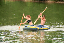 Hier sehen Sie wie 2 Personen in einem Schlauchboot über den See paddeln.
